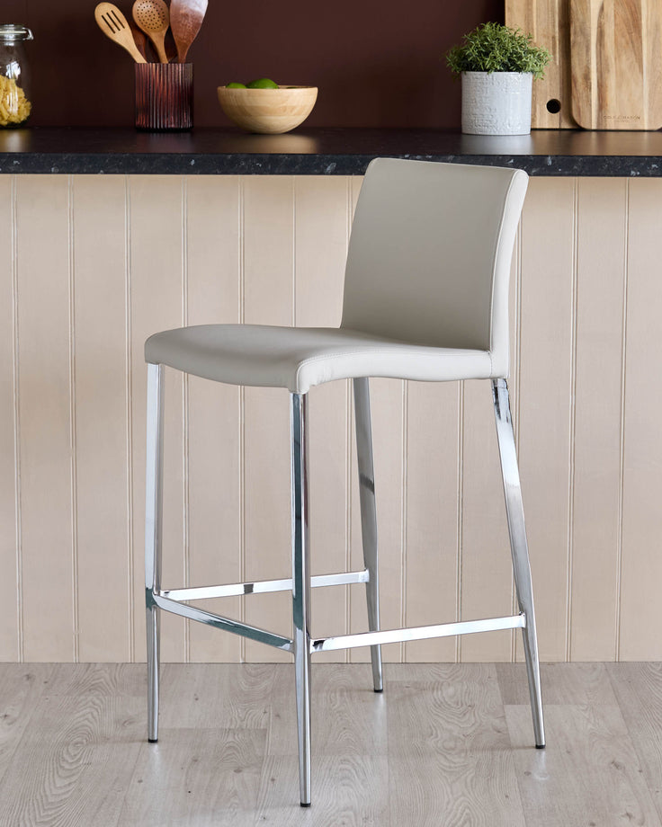 A modern bar stool with a pale grey seat and chrome legs, set against a kitchen backdrop.