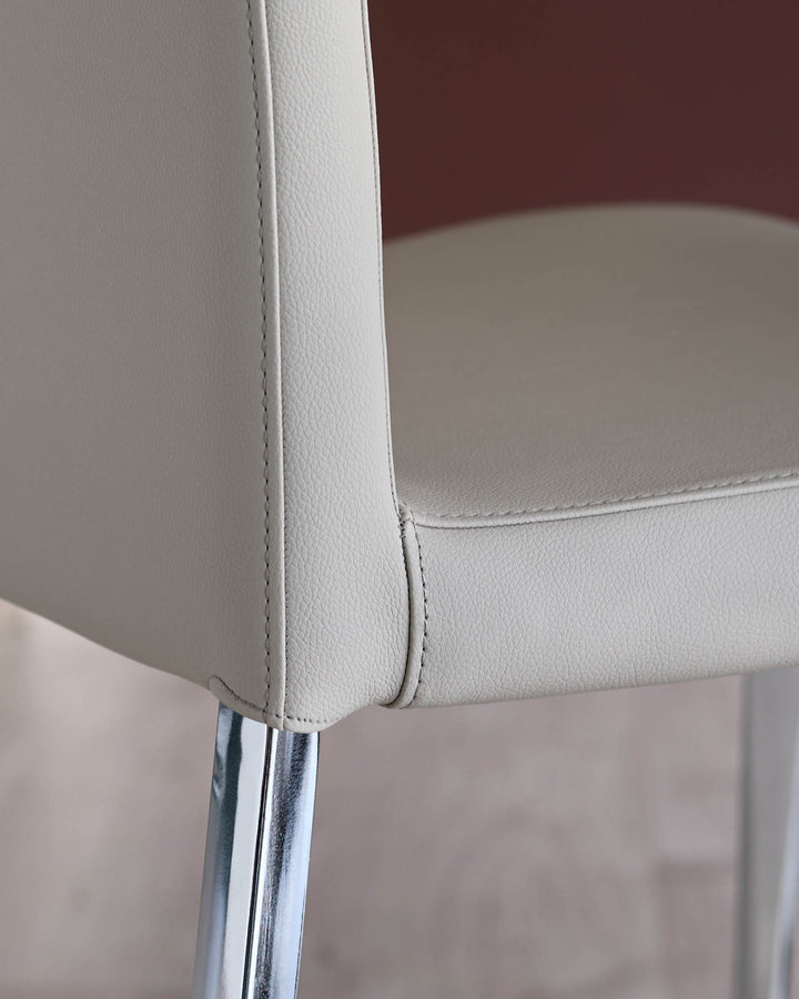 Close-up of a stylish chair featuring cream leather upholstery and chrome legs, ideal for a modern dining or office setting.