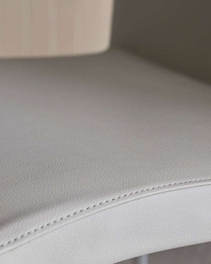 Close-up of a textured, light grey leather seat with stitched detailing. Part of a modern chair.