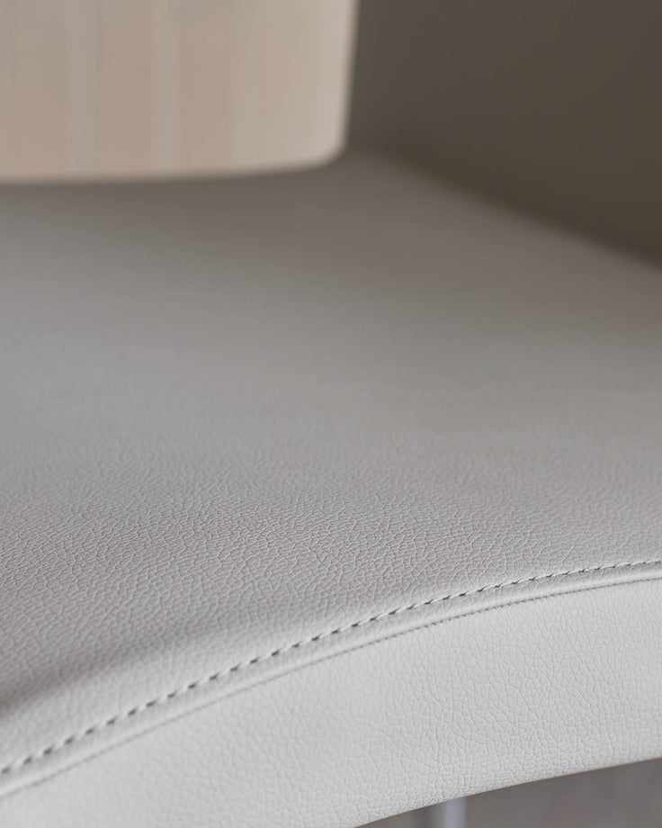 Close-up of a textured, light grey leather seat with stitched detailing. Part of a modern chair.