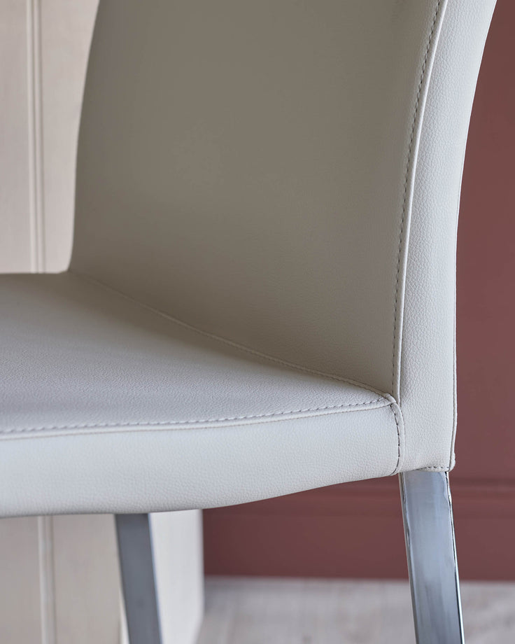 Close-up of a sleek, modern chair with a light grey leather seat and backrest, and polished chrome legs.