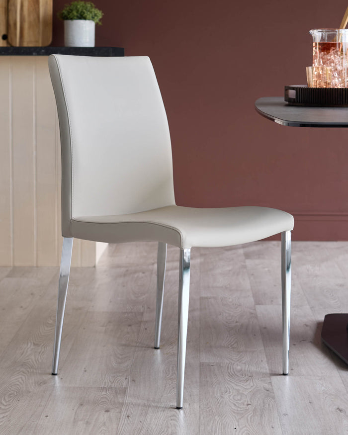 A stylish light grey chair with chrome legs sits on a light wooden floor. A table and decorative items are partially visible.
