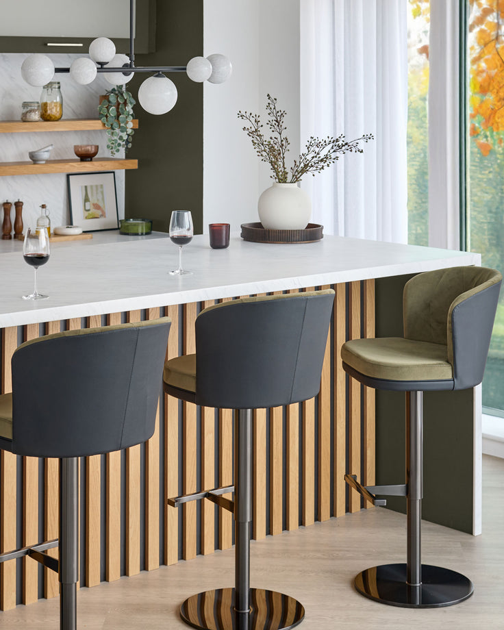 Elodie gas lift bar stool in olive green and black velvet, shown at modern kitchen island with striped wood paneling.
