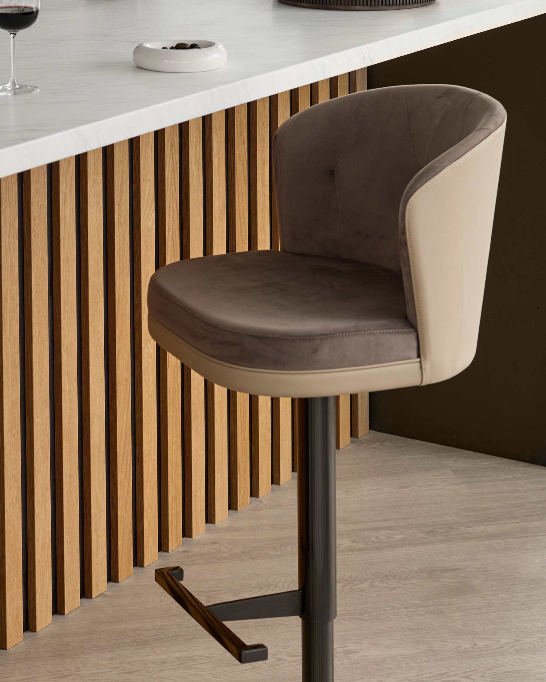 Elodie gas lift bar stool in mocha velvet and natural faux leather, shown at a kitchen counter with vertical wood paneling.