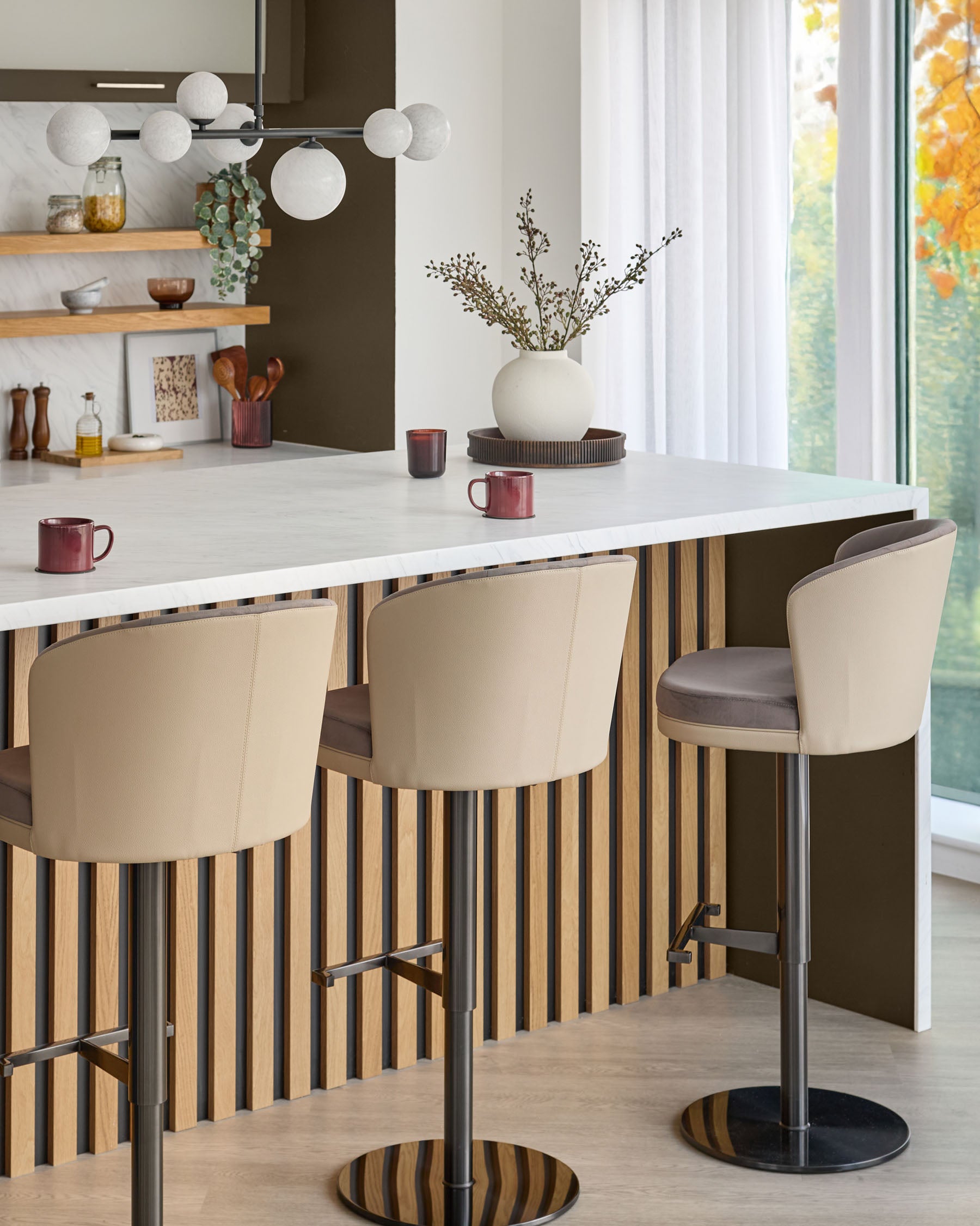 Elodie gas lift bar stool in mocha velvet with natural wood striped base and footrest, shown in modern kitchen setting.
