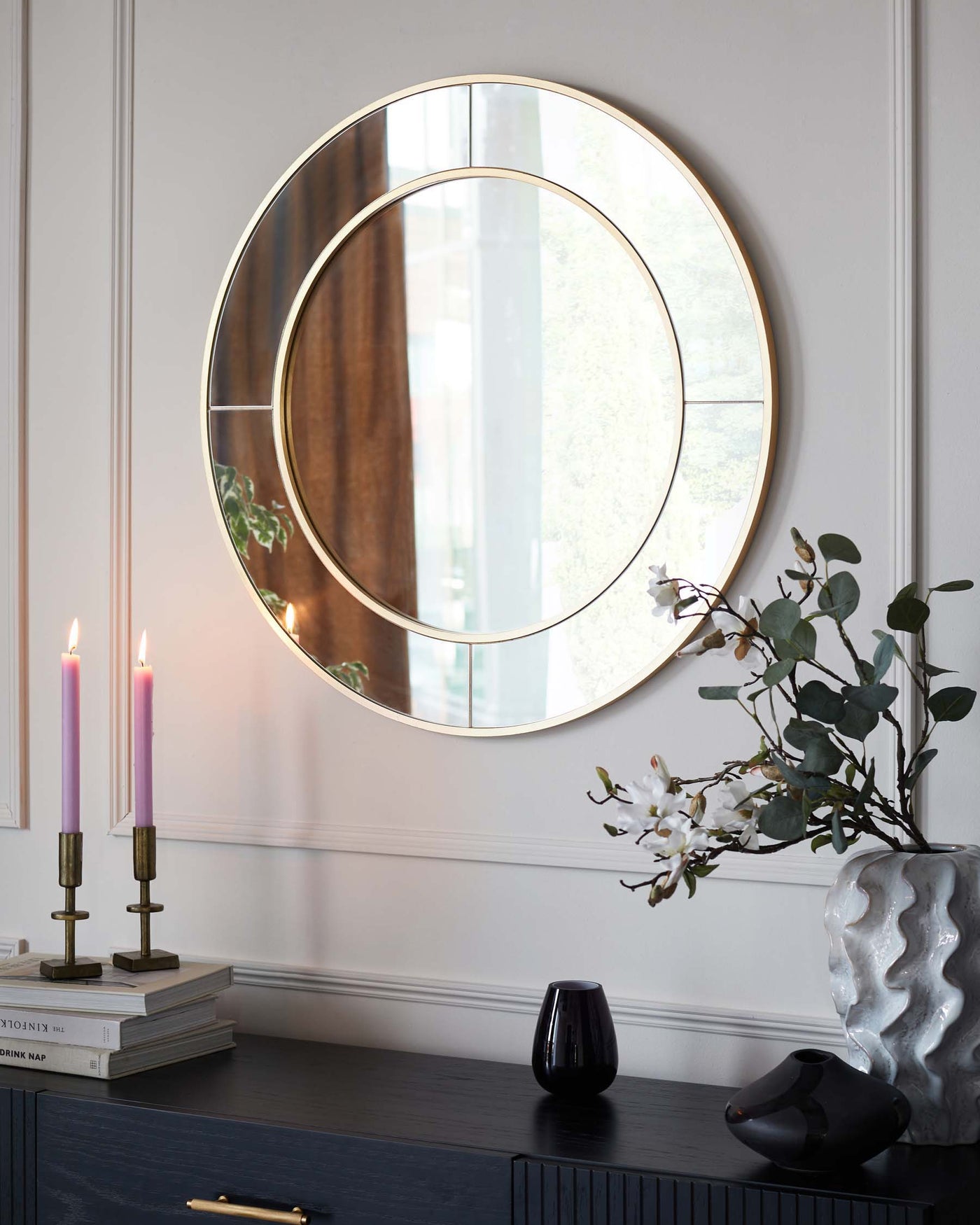 Elegant dark-toned wooden sideboard with brass handles, featuring a textured front design, complemented by a large round mirror with a slim golden frame mounted above it.
