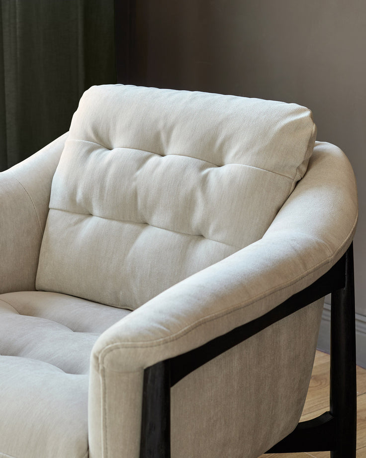 Cream fabric accent chair with black wooden frame and quilted backrest cushion, shown from side angle.
