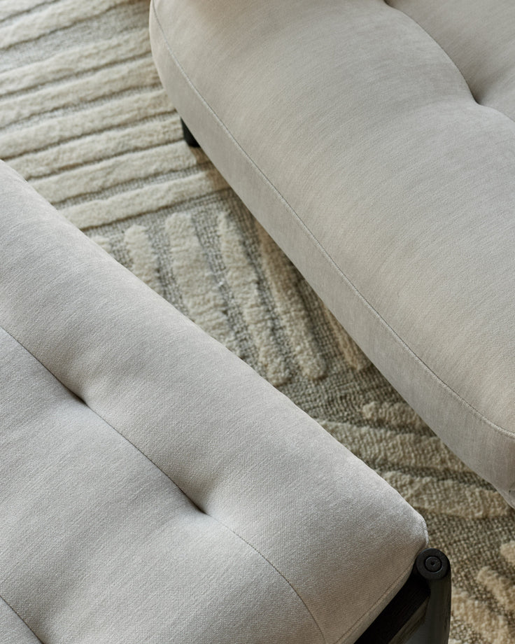 Ember accent chair with footrest in light grey fabric, showing close-up of upholstered seat and black leg detail on neutral area rug.