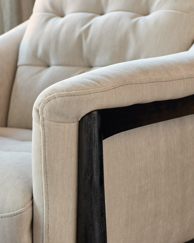 Close-up of cream fabric armchair with dark wood frame and rolled armrest detail.