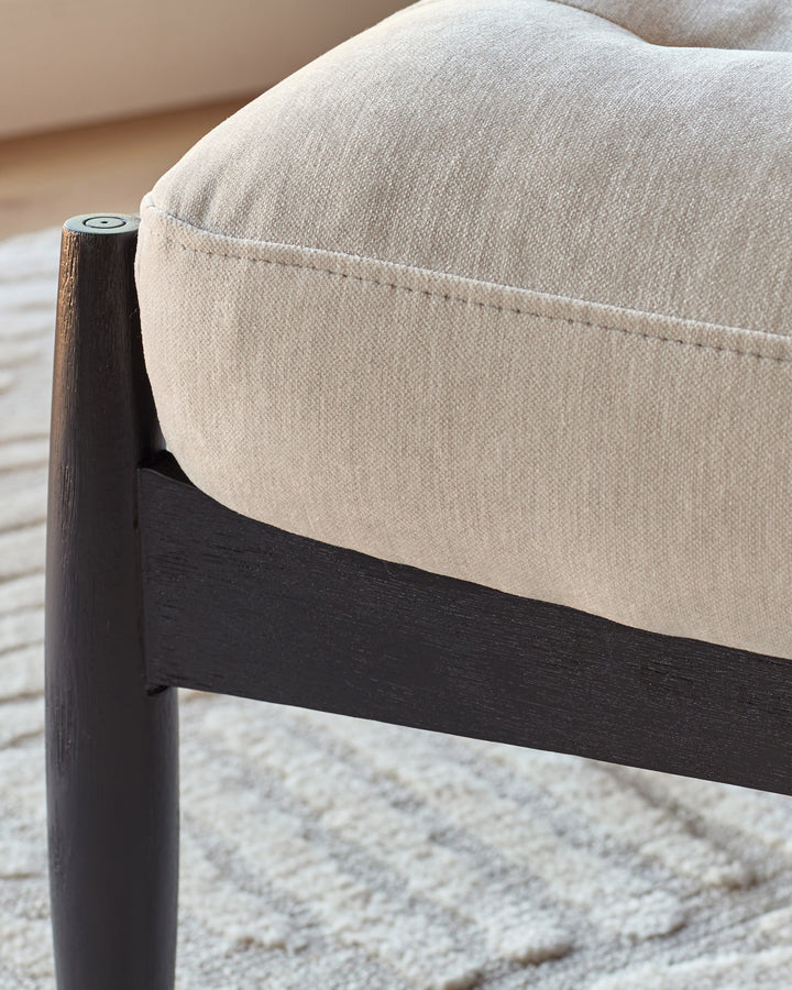 Ember accent chair with dark wood frame and beige fabric upholstery, shown in close-up detail of armrest and seat.