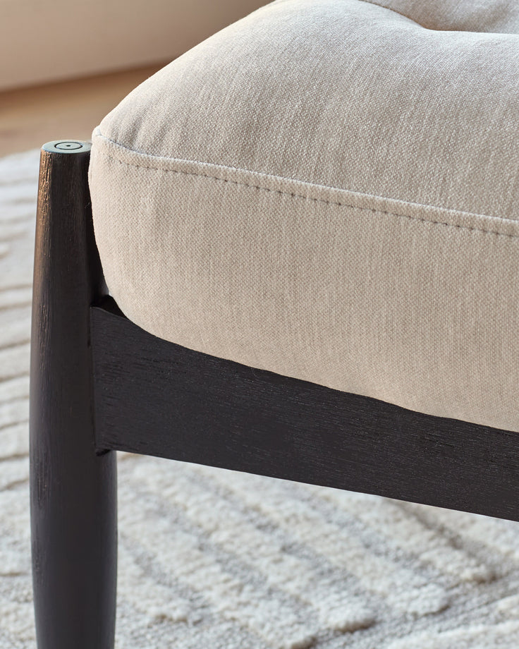 Ember accent chair with dark wood frame and beige fabric upholstery, shown in close-up detail of armrest and seat.