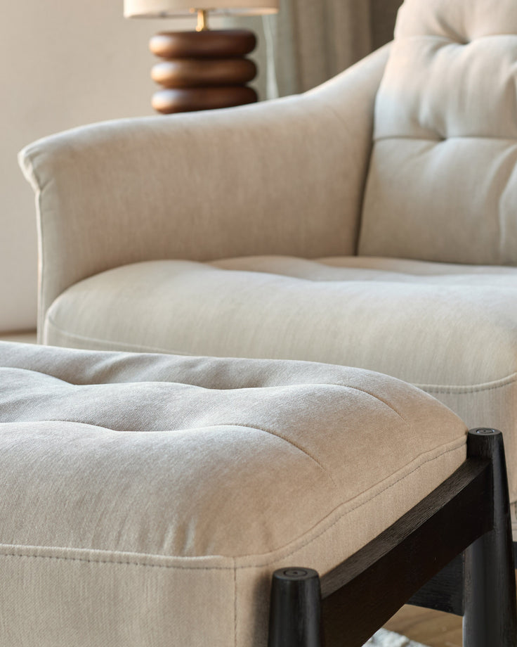 Ember accent chair with footrest in grey fabric, showing quilted seat cushion and black wooden legs from a side angle.