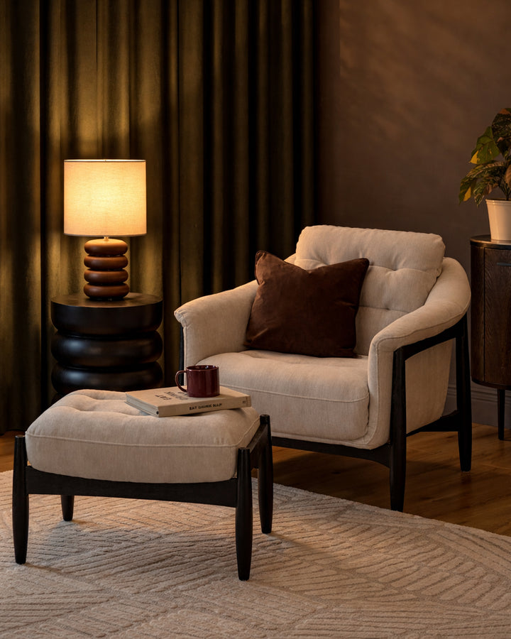 Ember accent chair with footrest in grey fabric, black wooden frame, paired with matching ottoman in a warm, styled living room setting.
