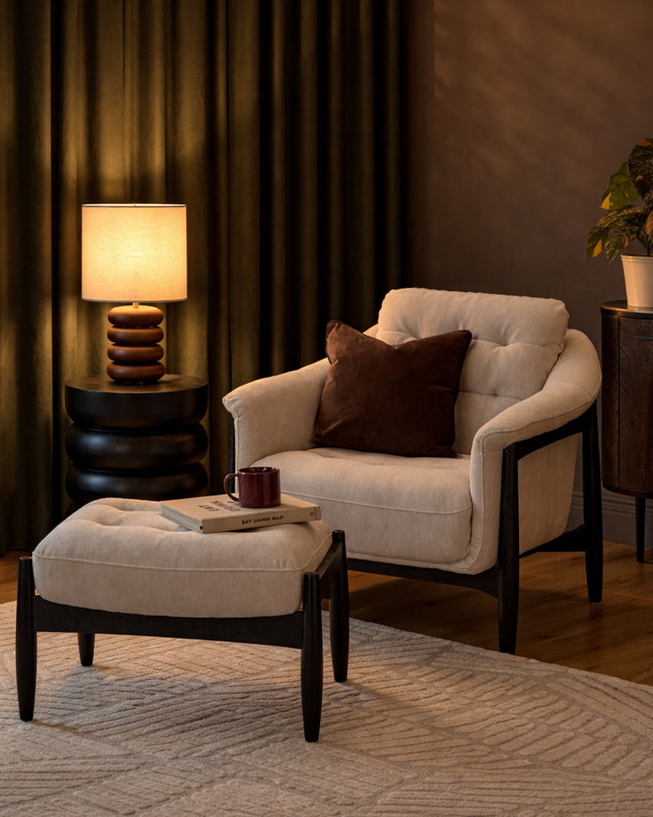Ember accent chair with footrest in grey fabric, black wooden frame, paired with matching ottoman in a warm, styled living room setting.