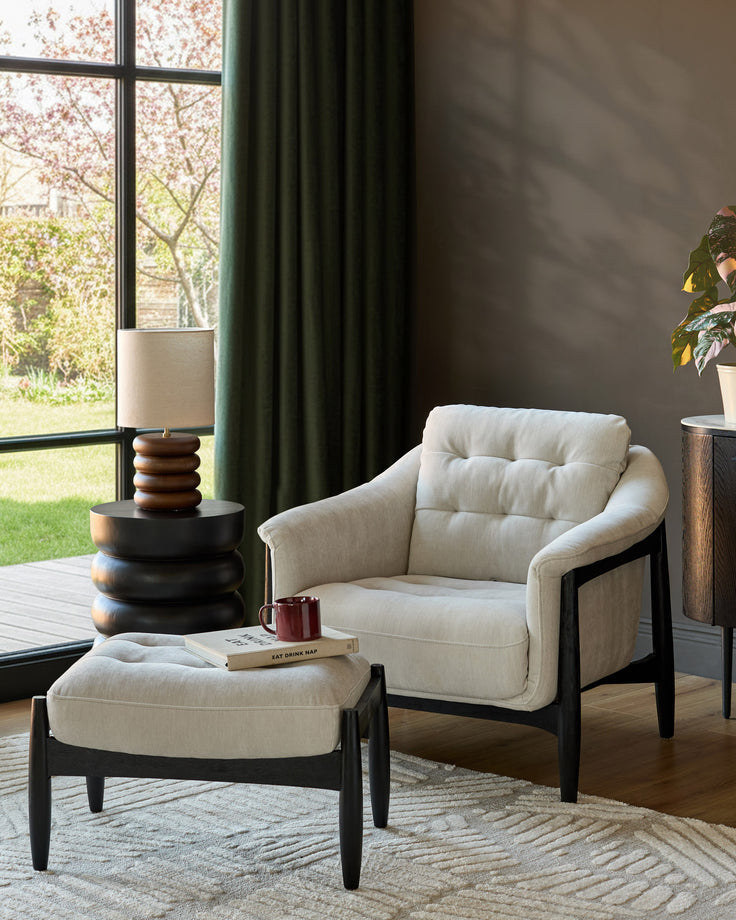 Ember accent chair with footrest in grey fabric, black wooden frame, positioned in a modern living room setting.