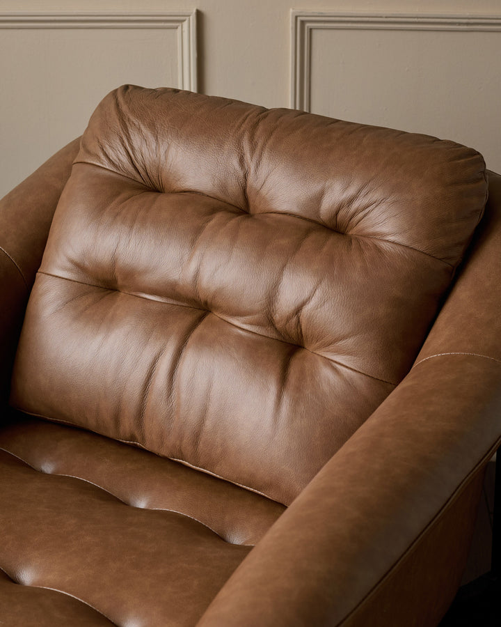 Tan leather accent chair with tufted backrest and armrests, shown in close-up detail against neutral wall.