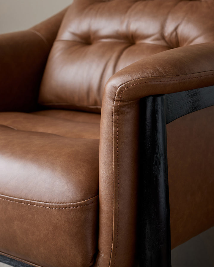 Tan leather accent chair with black wooden frame and armrest, detailed close-up view showing stitching and cushioned seat.