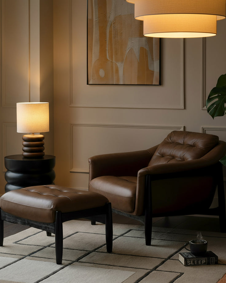 Tan leather accent chair with black wooden legs and matching quilted footrest in a modern living room setting.