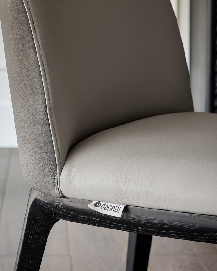 Emerson dining chair in light grey leather with dark grey accents, featuring a black wood frame, close-up side view.
