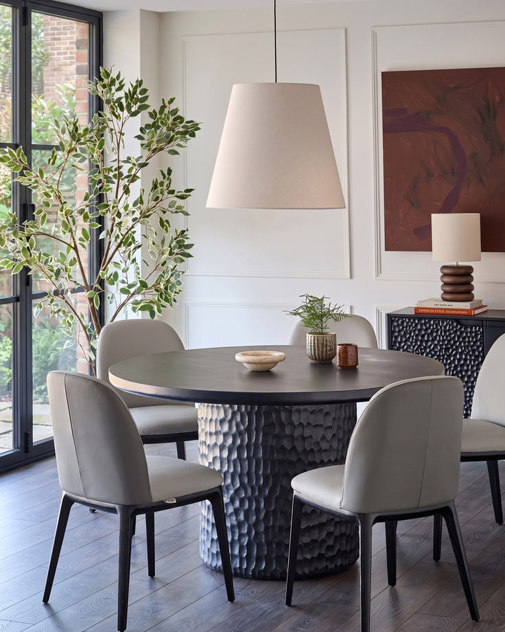 Emerson dining chair in light grey leather, shown at round black table with two chairs visible in modern dining room setting.