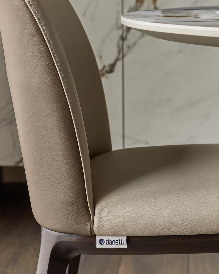 Close up of a modern light brown leather chair with dark wood frame and a white "danetti" label on the side.