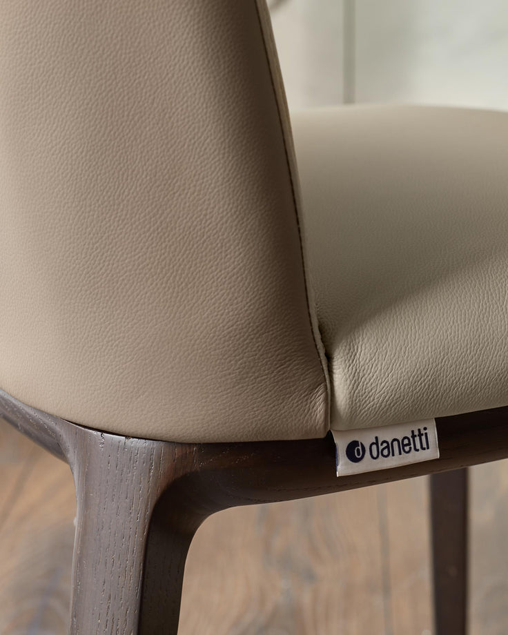 Close up of a modern leather chair, with a wooden frame and a 'Danetti' label.