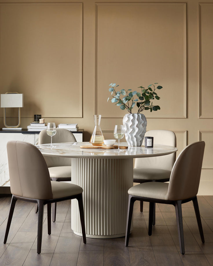 A round marble dining table with four neutral-toned chairs. A modern, minimalist design for a contemporary dining space.