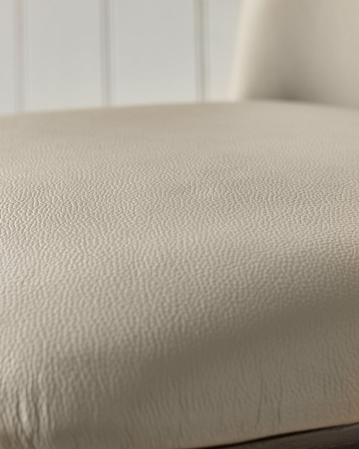 Close-up of a beige leather chair seat, showing texture and soft curves for comfort and style.