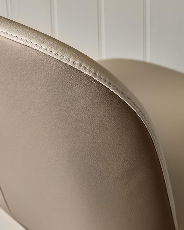 Close-up of a beige leather chair, showing the texture and stitching detail.