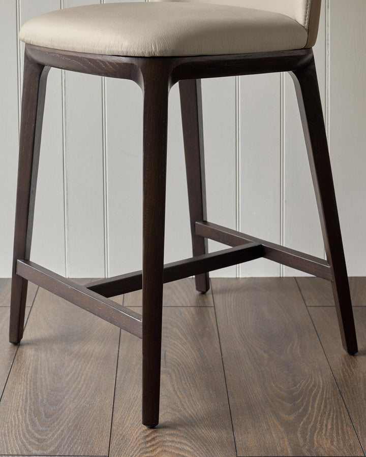 Close-up of a brown wooden stool with a beige cushioned seat, showcasing its design and sturdy construction.