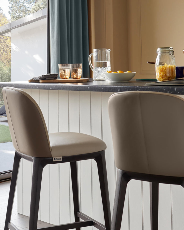 Two Danetti bar stools with beige seats and dark wood frames sit at a kitchen counter, adding style to the space.