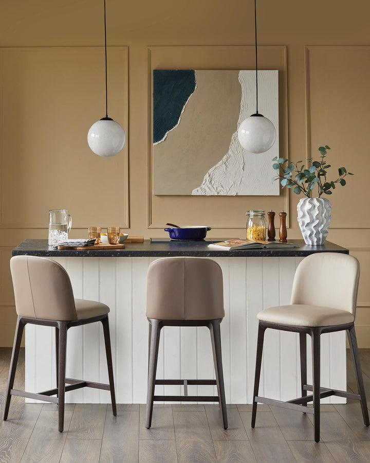 Three stylish bar stools with wooden frames and neutral coloured seats sit at a kitchen island.