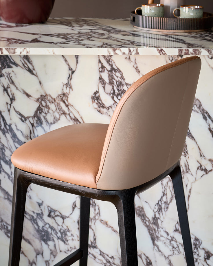 Tan leather Emerson bar stool with dark wood legs, shown from back angle at marble-topped counter.