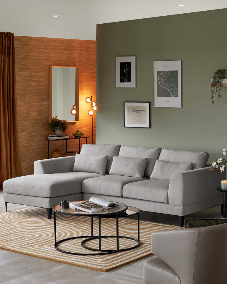Contemporary L-shaped sectional sofa in light grey fabric with slender legs, accompanying round black nesting coffee tables with glass tops, and a small wooden sideboard with a dark finish against the wall.