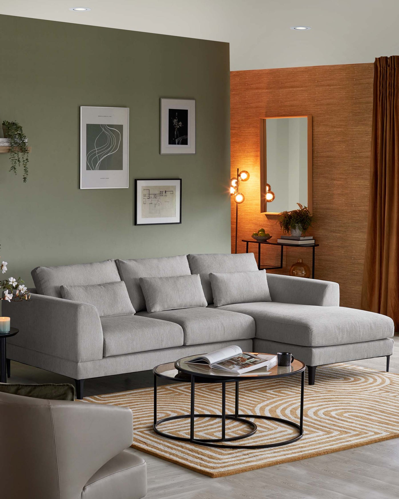 A contemporary light grey sectional sofa with clean lines and plush cushions, paired with a set of nesting round coffee tables featuring black metal frames and glass tops, displayed in a modern living space.