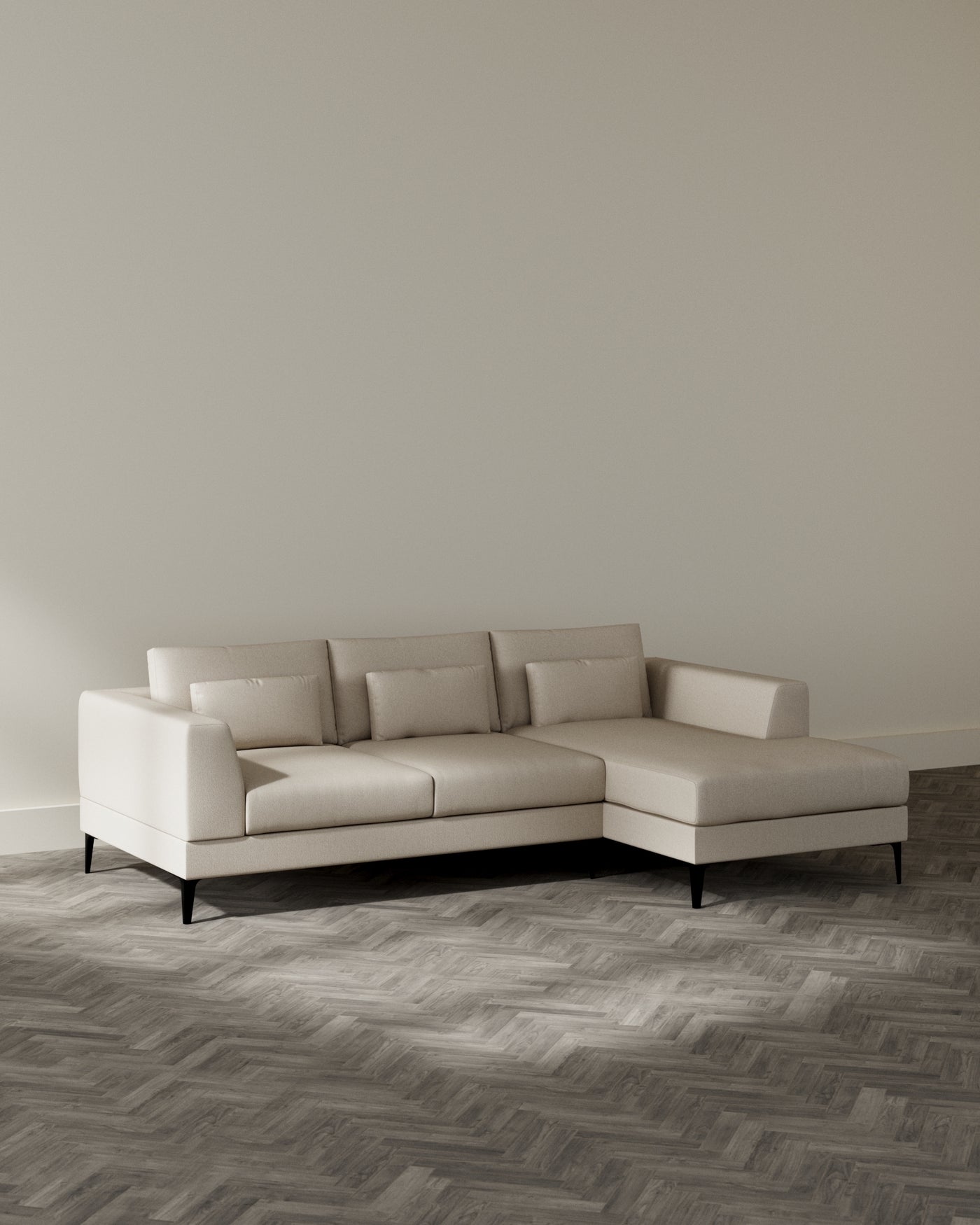 Modern beige sectional sofa with chaise lounge and black tapered legs positioned in a room with herringbone hardwood flooring against a soft grey wall.