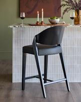 Black leather bar stool with curved backrest and black wooden legs, positioned at white tiled counter in modern dining setting.