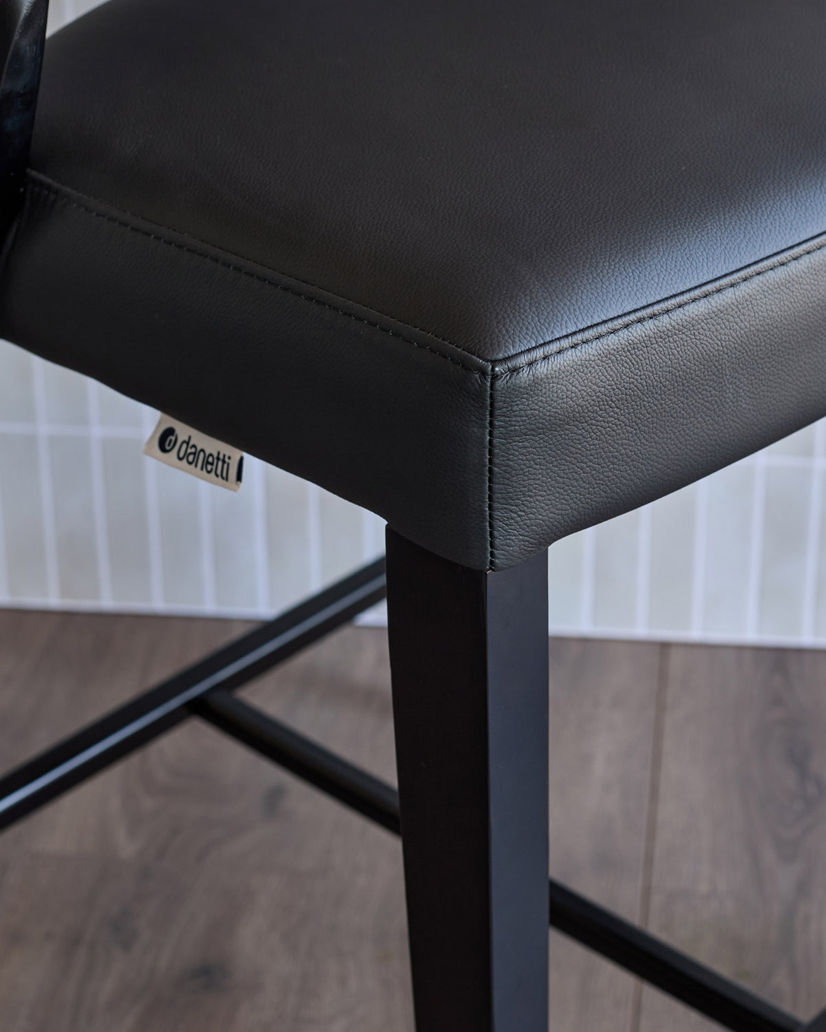 Enzo bar stool in black leather, detail view showing seat cushion, metal leg frame and designer label.