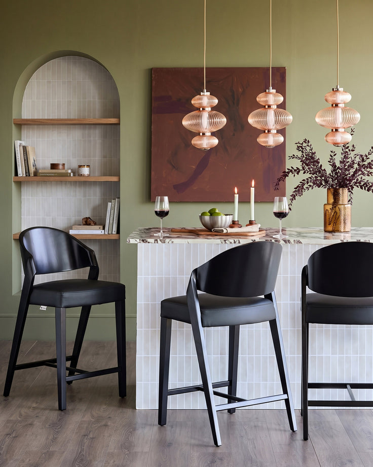 Enzo black leather bar stool with curved backrest, shown at kitchen counter in modern dining setting.