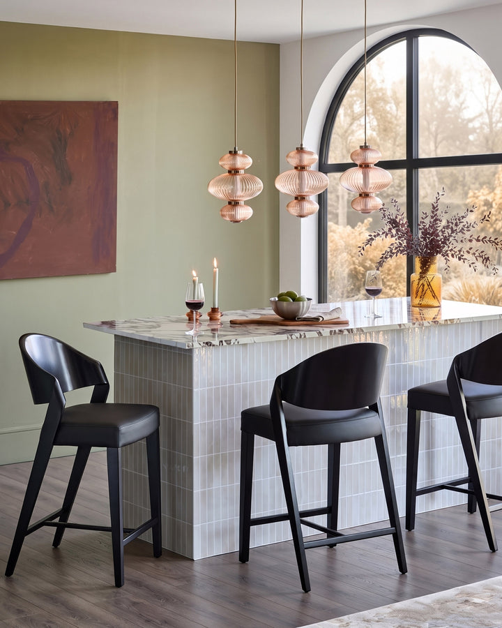 Enzo black leather bar stool shown in modern dining space with marble counter and pendant lights.