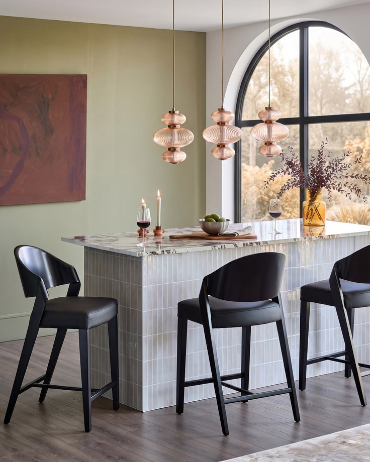 Enzo black leather bar stool shown in modern dining space with marble counter and pendant lights.