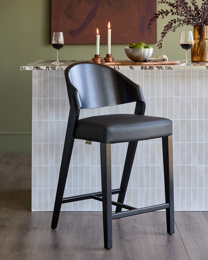 Black leather bar stool with curved backrest and wooden legs, positioned at white tile counter in styled dining setting.