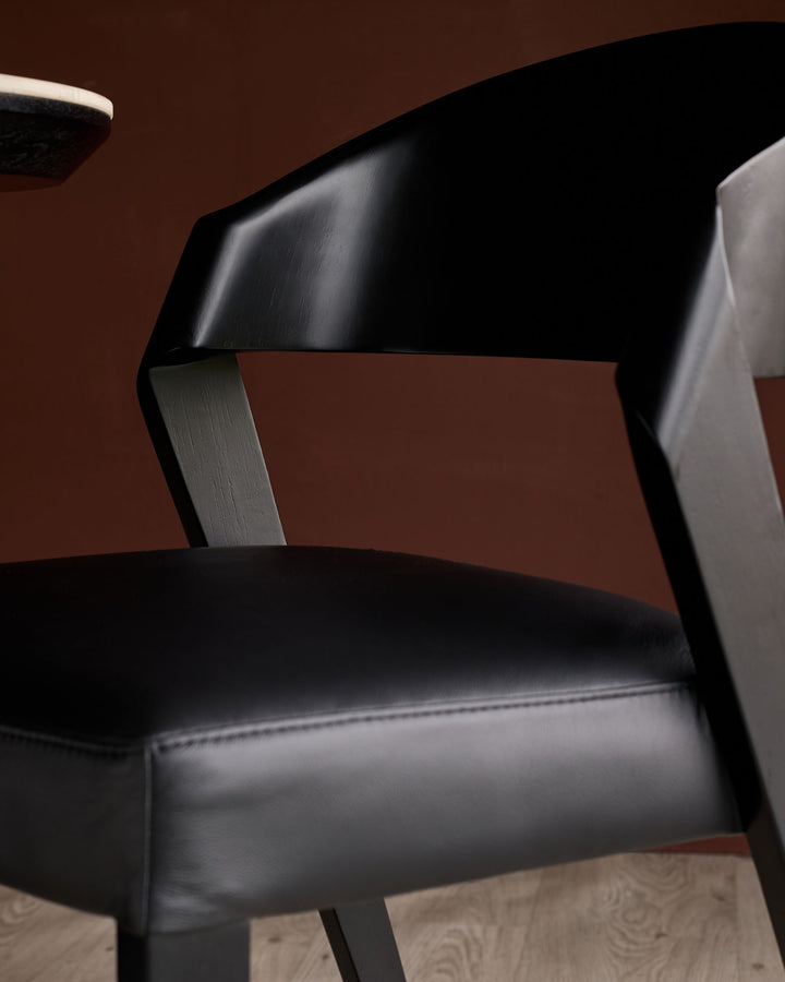 Black leather dining chair with curved backrest and metal frame, shown from side angle against brown background.