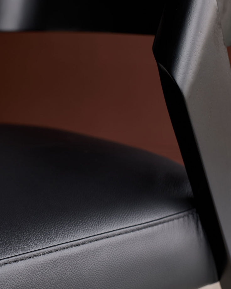 Enzo dining chair in black leather, close-up of seat and backrest showing textured leather finish and curved design details.