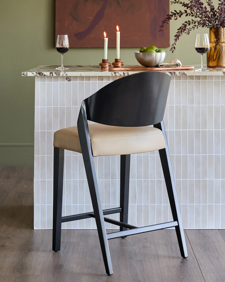Enzo bar stool in natural leather with black frame, shown at marble-top bar counter in styled dining setting.