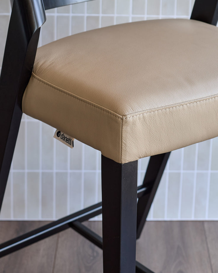 Enzo bar stool in natural leather with black metal frame, shown in close-up detail of seat and legs.