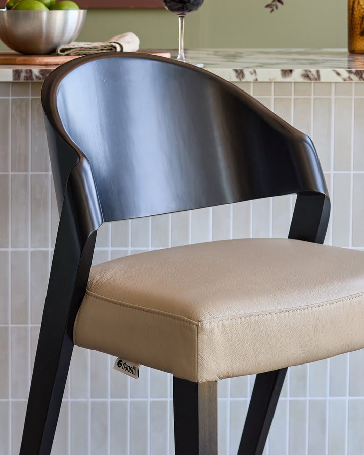 Enzo bar stool with brushed metal backrest, cream leather seat, and black wooden legs, shown at an angle.