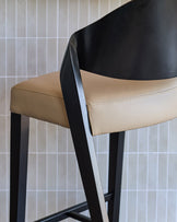Enzo bar stool in natural leather with black curved backrest and black metal frame, side view.
