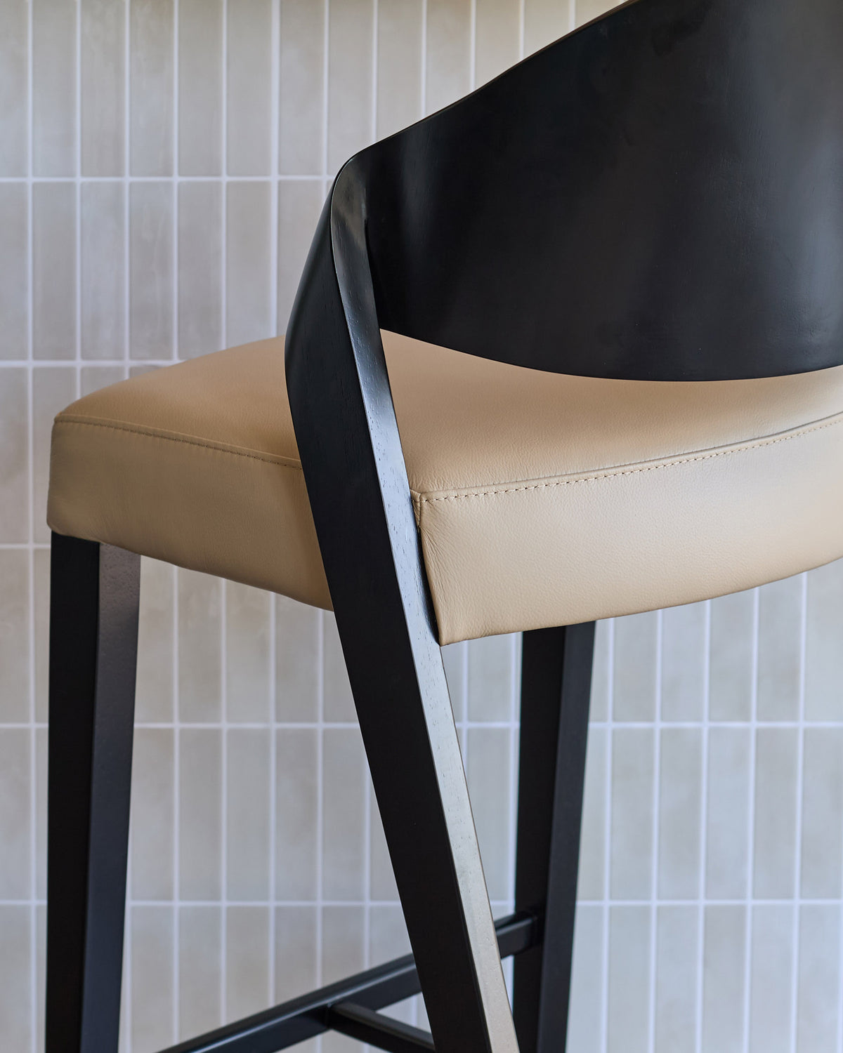 Enzo bar stool in natural leather with black curved backrest and black metal frame, side view.