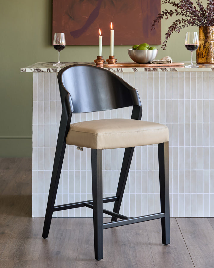Enzo bar stool in natural leather with black wood frame, shown at white marble counter with wine glasses and candles.